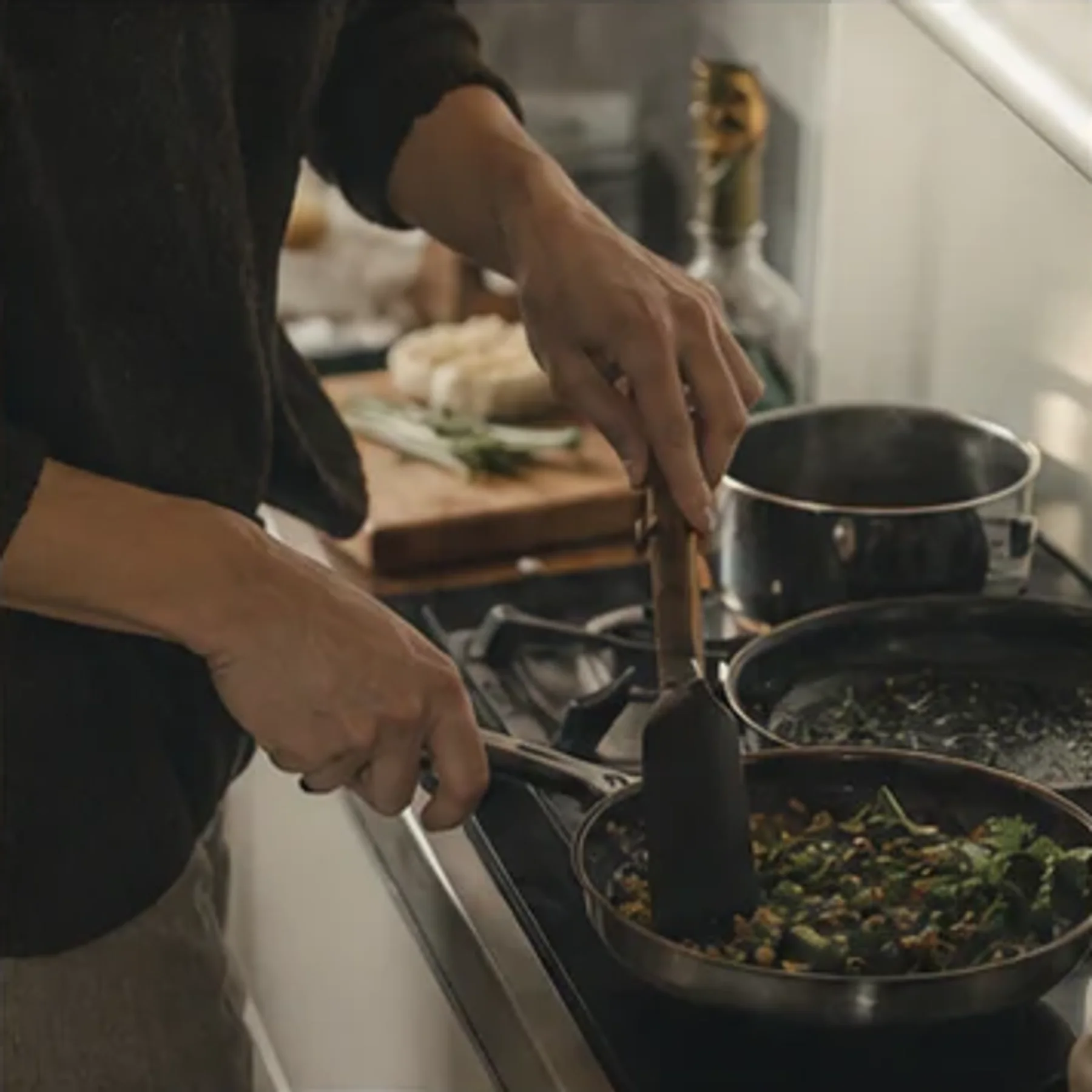 Hands preparing food at a kitchen stove.